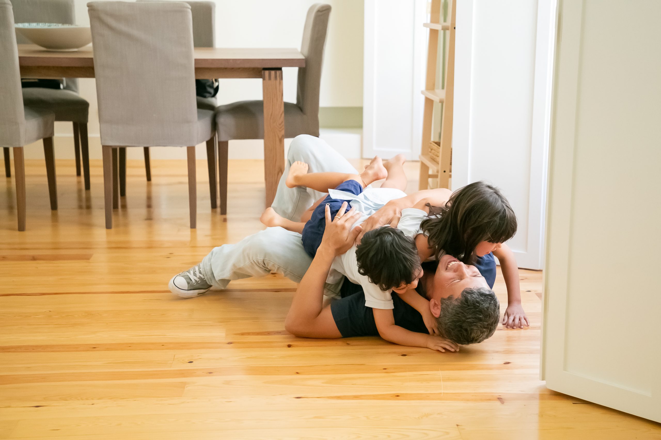laughing father lying floor hugging cute children scaled
